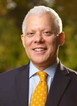 Portrait of Allen M. Omoto wearing a light blue shirt, navy jacket, and orange tie with the pitzer tree as a pattern